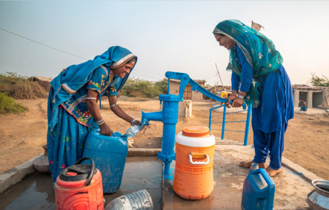 two smiling women filling water containers from a hand pump